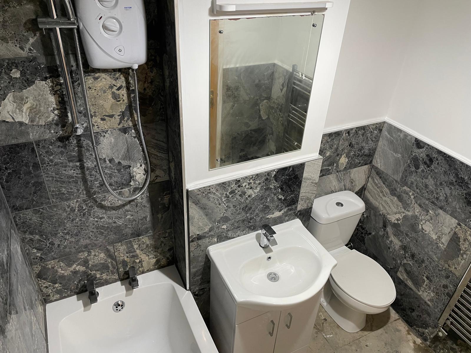 Bathroom with grey stone-effect tiling, electric shower, and bath